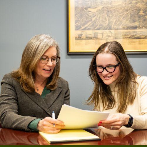 Attorney Kate Cerrone seated at conference table with a woman looking at paperwork together